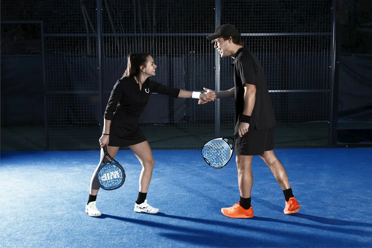 Two players tapping gloves on a floodlit padel court